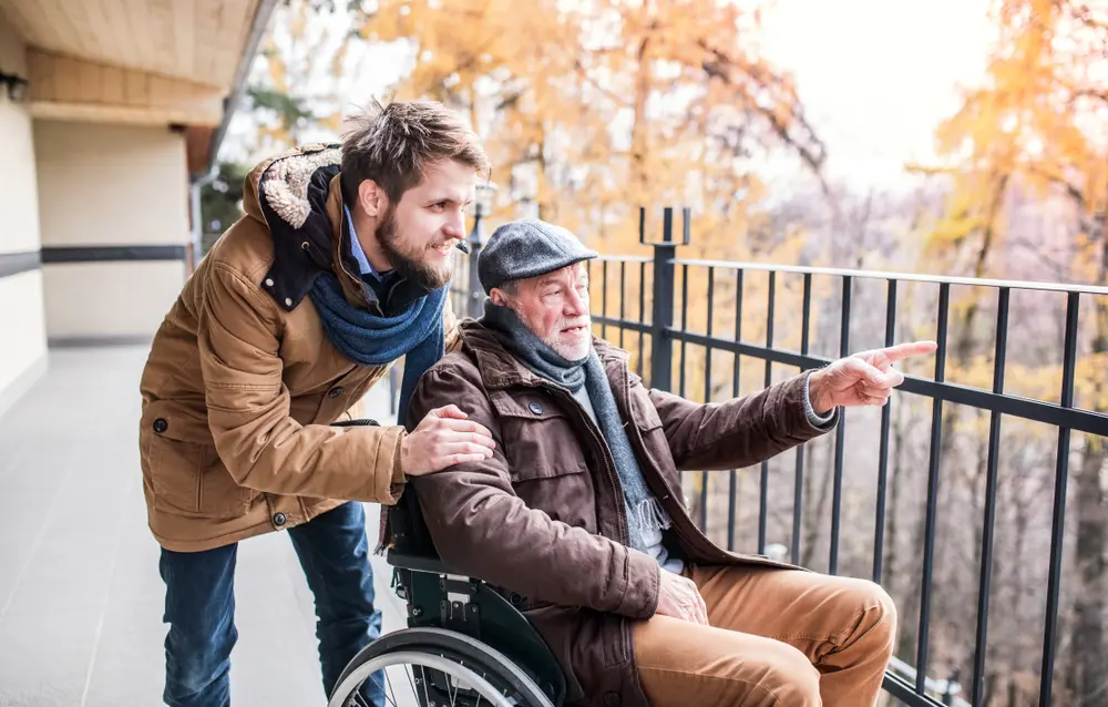 Young man with elderly man in wheelchair pointing at autumn trees.