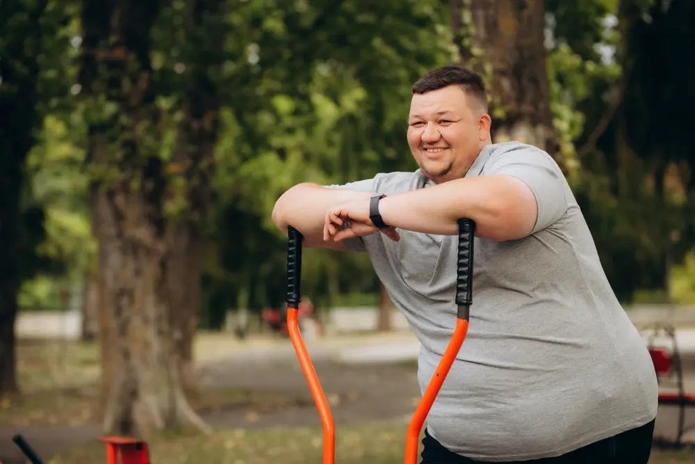 Smiling man using outdoor gym equipment to manage obesity