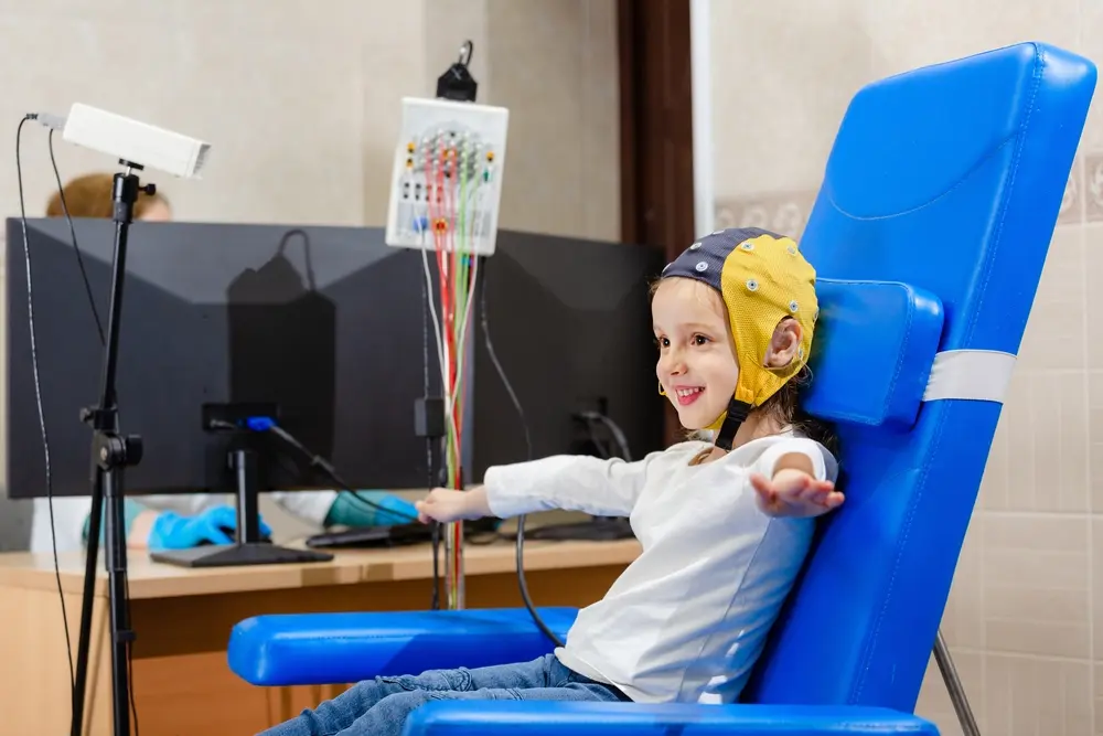 A smiling child wearing a medical head cap for a neurological exam in a clinic.