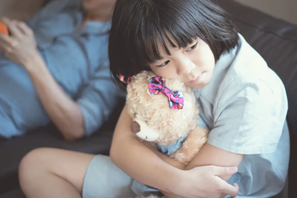 A young girl sitting on a sofa and hugging a plush teddy bear.