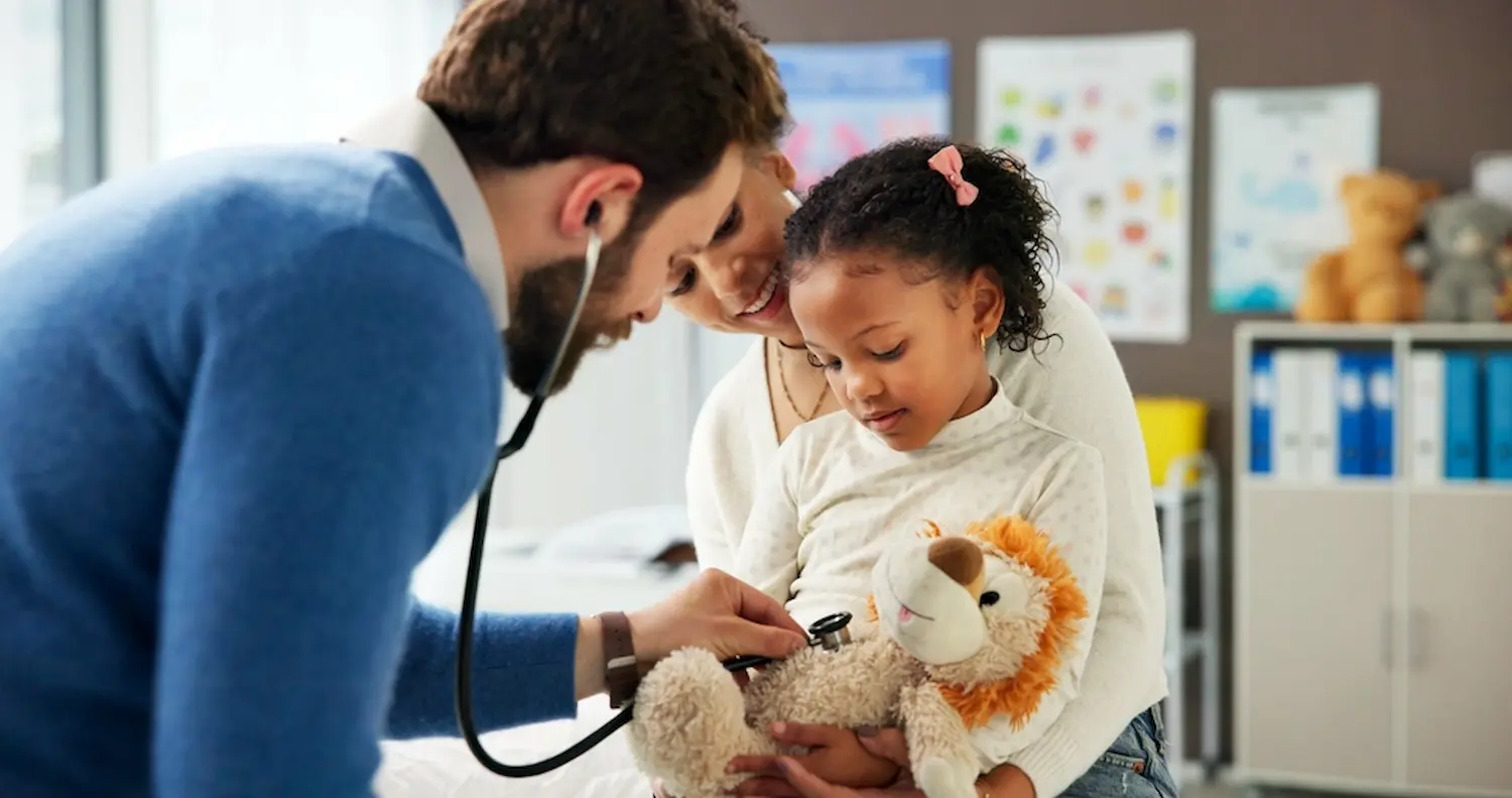 Pediatrician using a stethoscope on a young girl's stuffed lion toy.