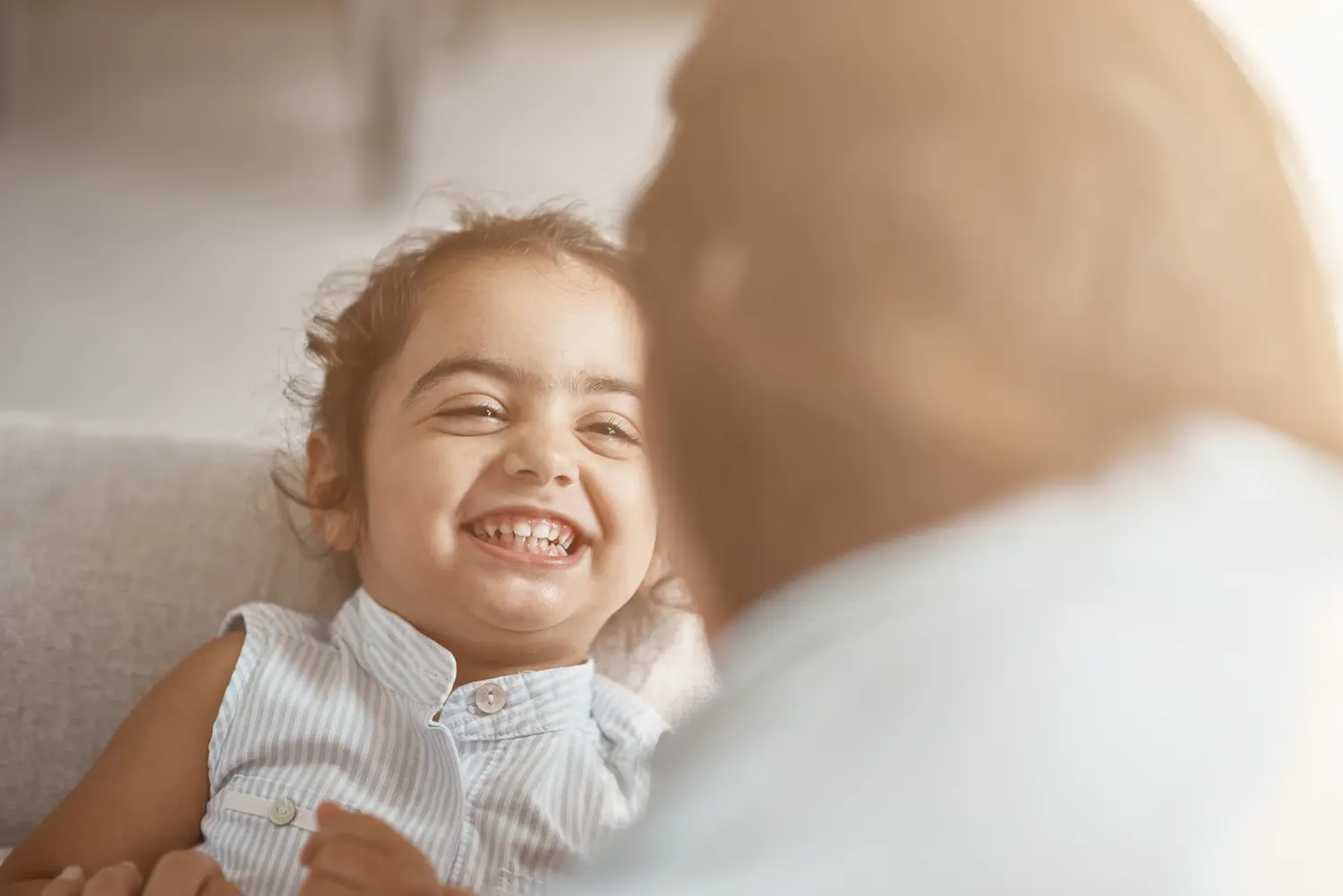 A young girl smiling brightly at her caregiver in a comfortable home setting, representing the improved quality of life and comfort that at-home LGS clinical trials aim to support.