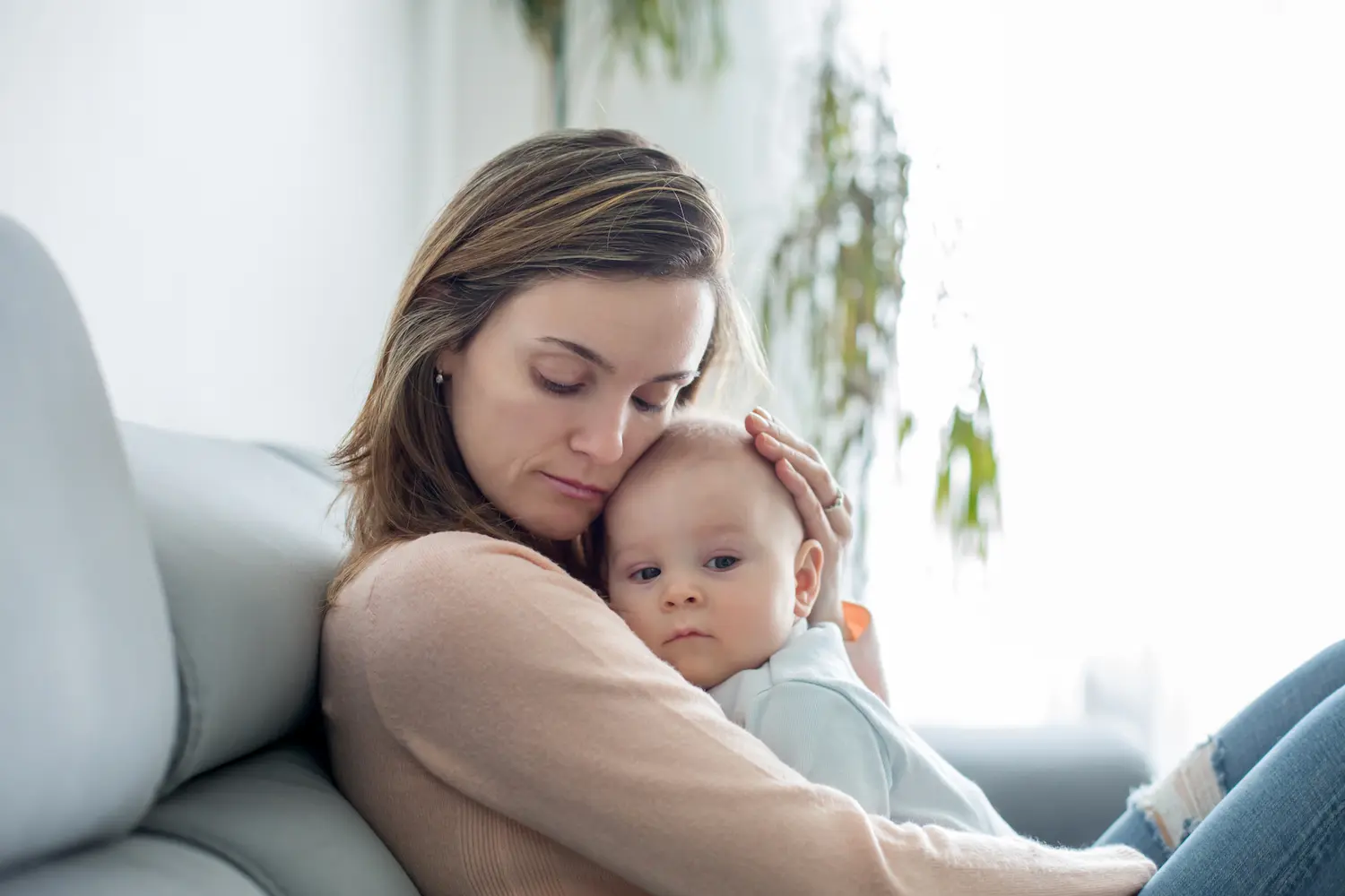 A mother sitting on a couch gently embracing her infant, reflecting the dedicated caregiver support required for families managing Dravet syndrome.